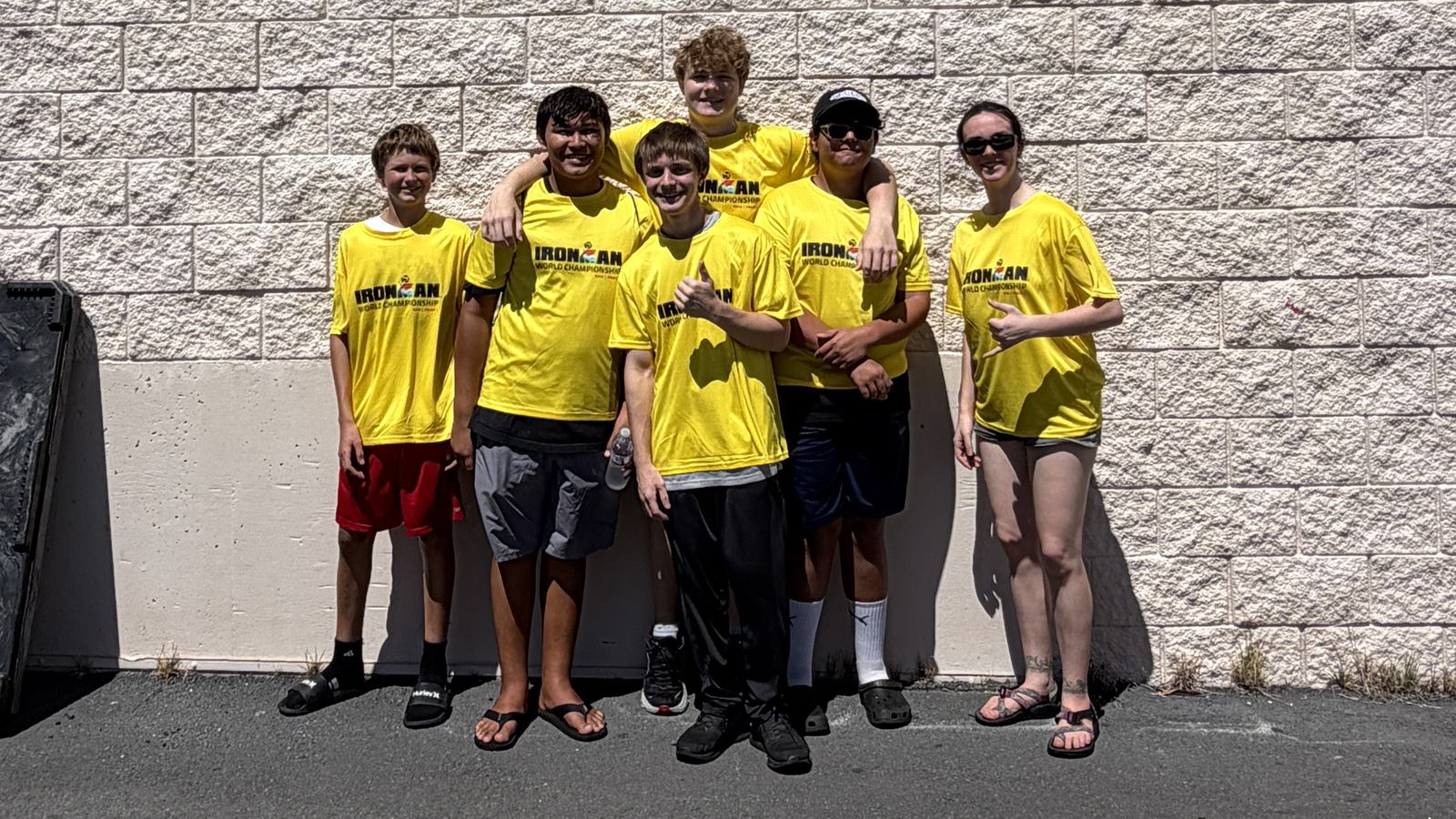 Six team members in yellow IRONMAN World Championship shirts standing together against a wall